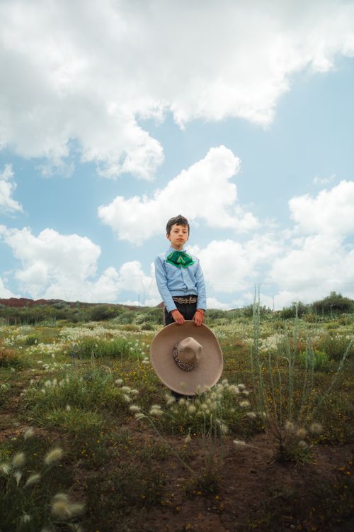 Free A young boy stands in a field in Hidalgo, México, wearing traditional Mexican attire with a wide-brimmed hat. Stock Photo