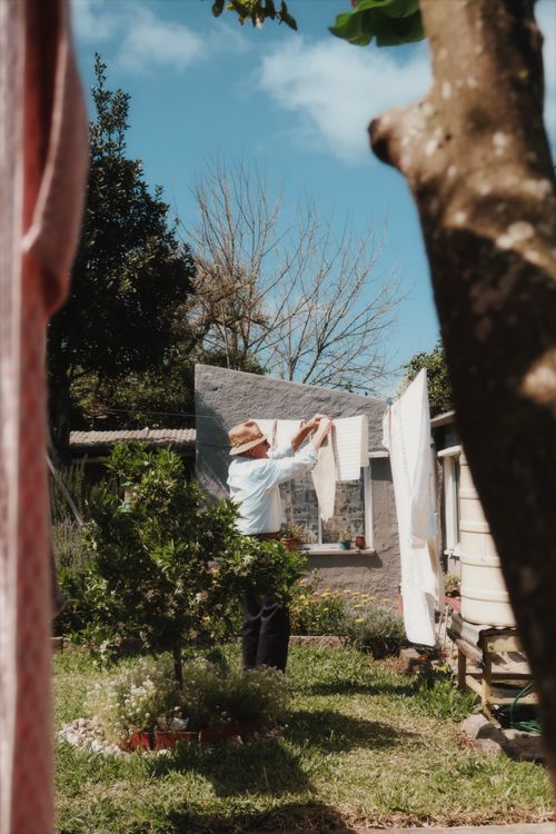 Free Elderly man hanging laundry outdoors in sunny garden in Melo, Uruguay. Stock Photo