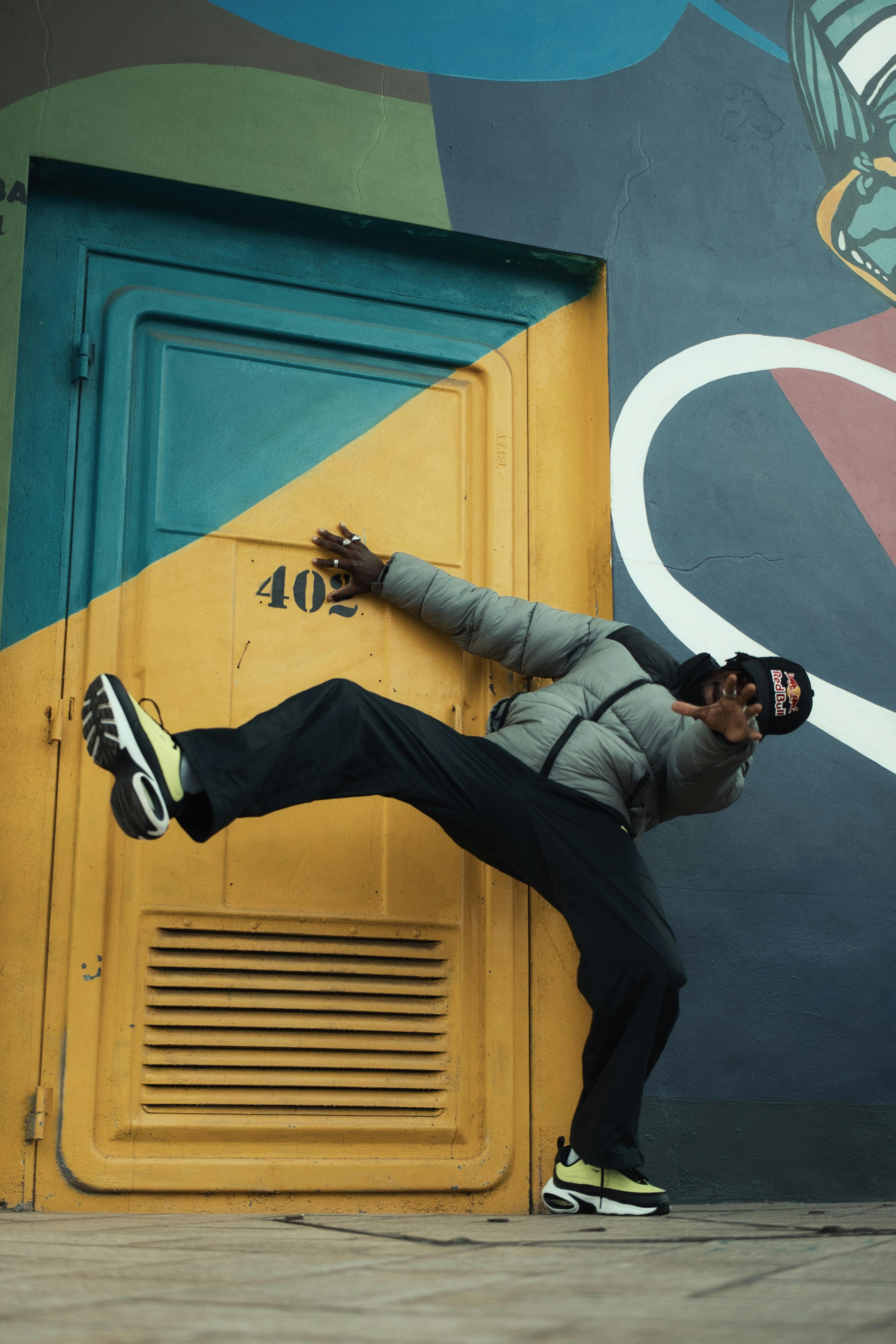A dynamic street dance pose against a colorful urban mural, showcasing athleticism and style.