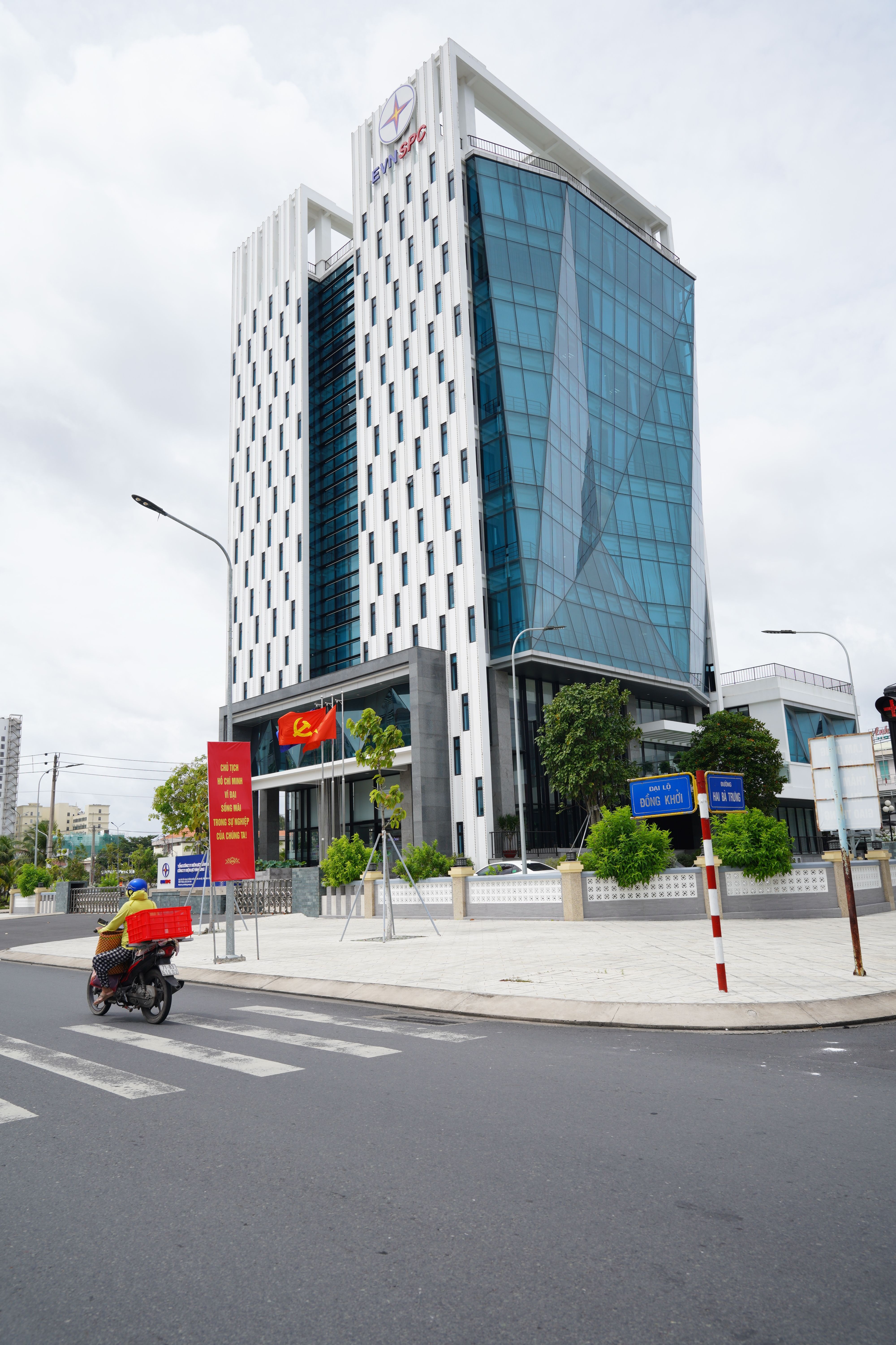 Tall glass-fronted office building with motorbike and street signs in urban setting.