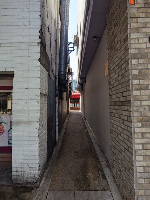 Free Narrow alleyway in an urban setting framed by brick walls and leading to a distant street view. Stock Photo