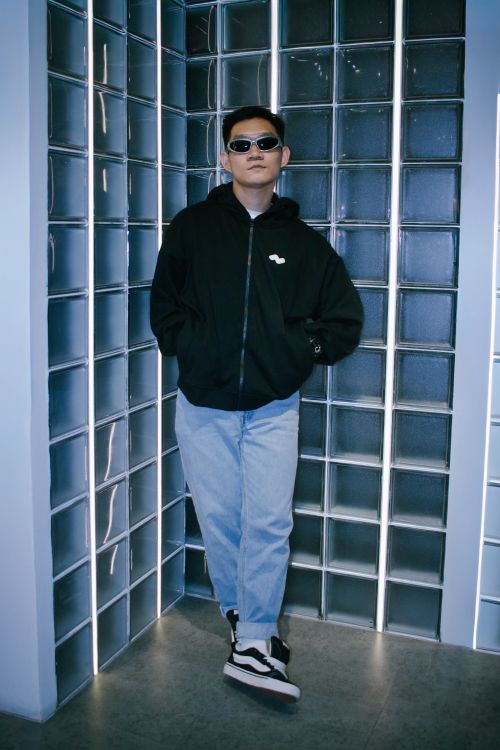 Free Confident young man in sunglasses and casual outfit leans against glass wall indoors. Stock Photo