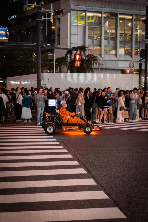 Free Vibrant night scene of a person in a kart costume crossing a Tokyo street, surrounded by onlookers. Stock Photo