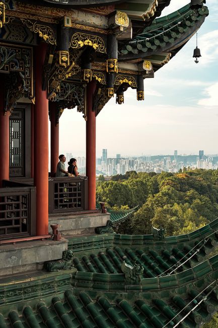 A couple enjoying the view from a traditional Chinese pavilion, overlooking a city skyline.