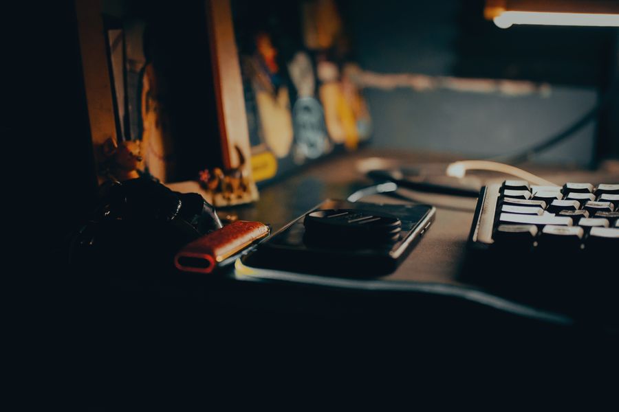 Dimly lit desk with a keyboard and gadgets in warm ambient light — photo by Justin Rieta on Pexels