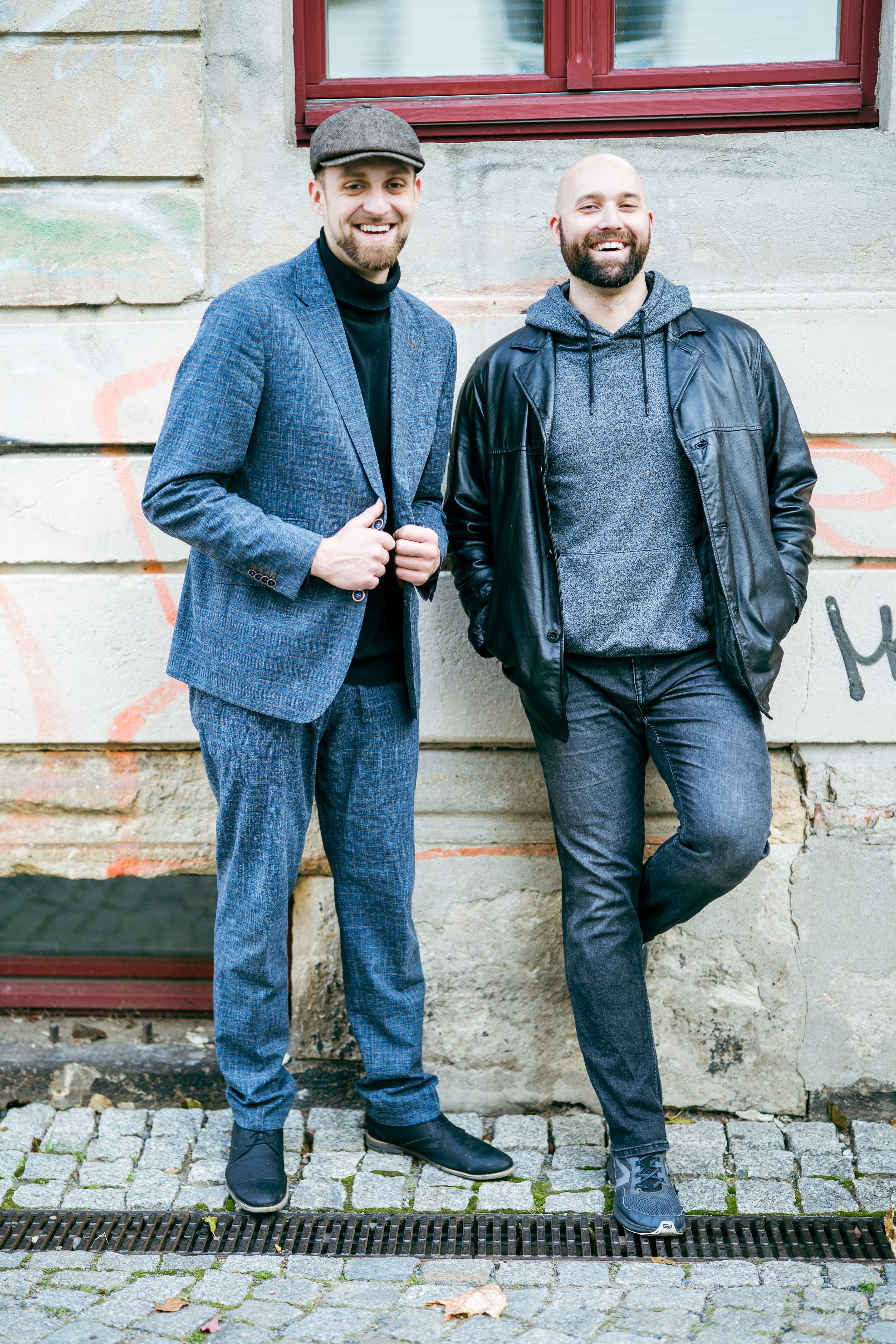Two stylish men pose casually against a graffiti wall in Dresden, showcasing modern street fashion.