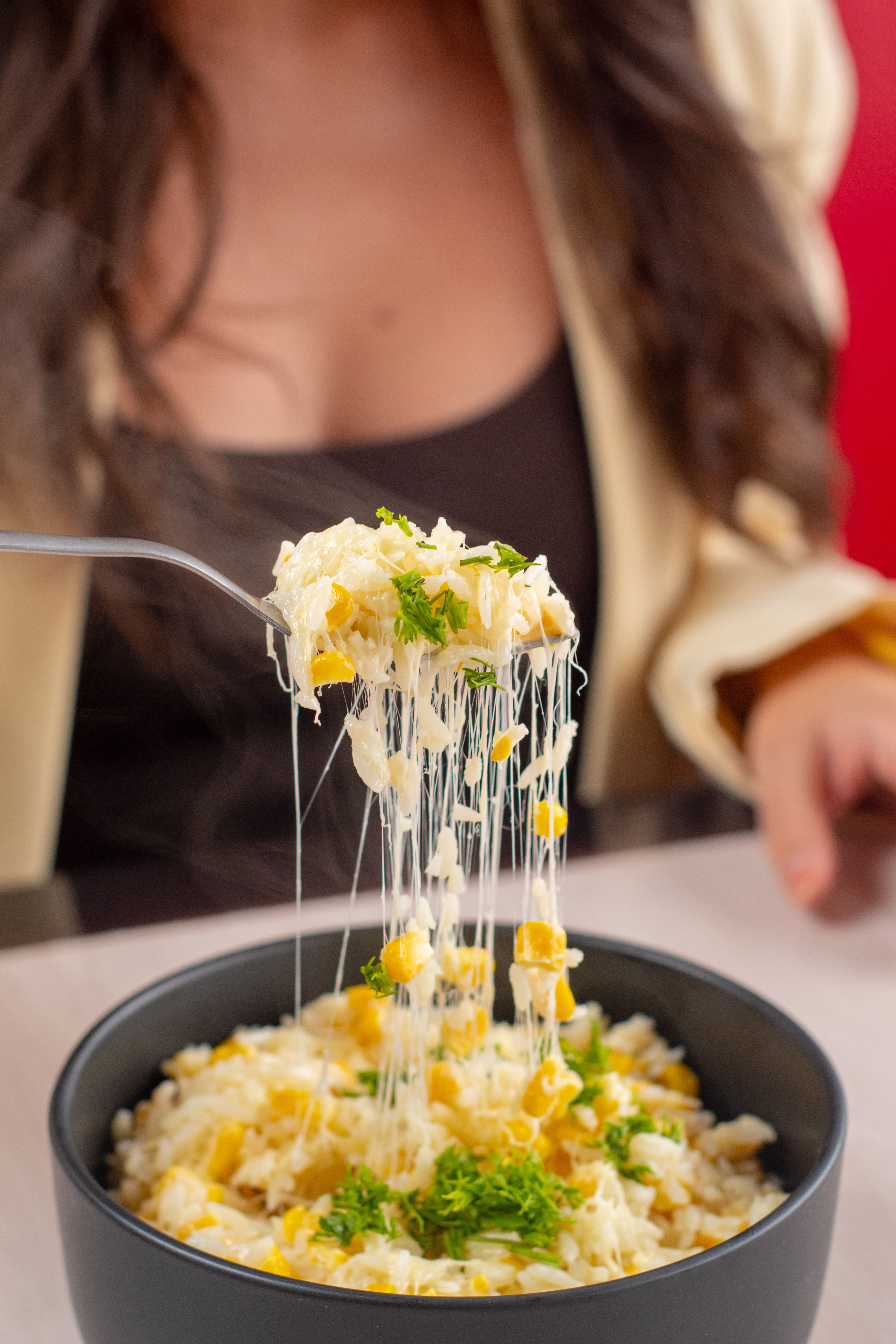 Close-up of a cheesy corn rice bowl with greenery and a person enjoying it in Guayaquil.