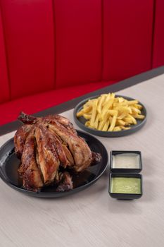 A plate of roasted chicken served with fries and two dips indoors.