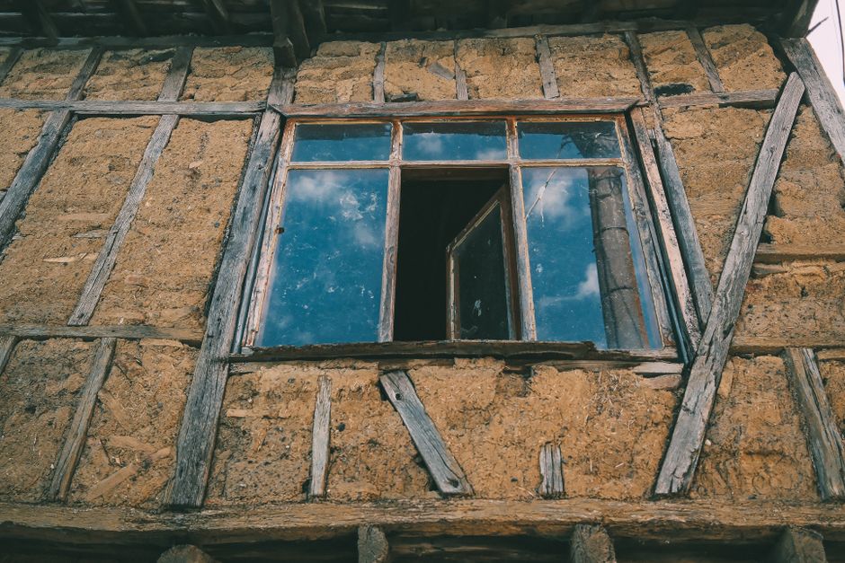 Image of a rustic cob house with an open window, reflecting the blue sky.