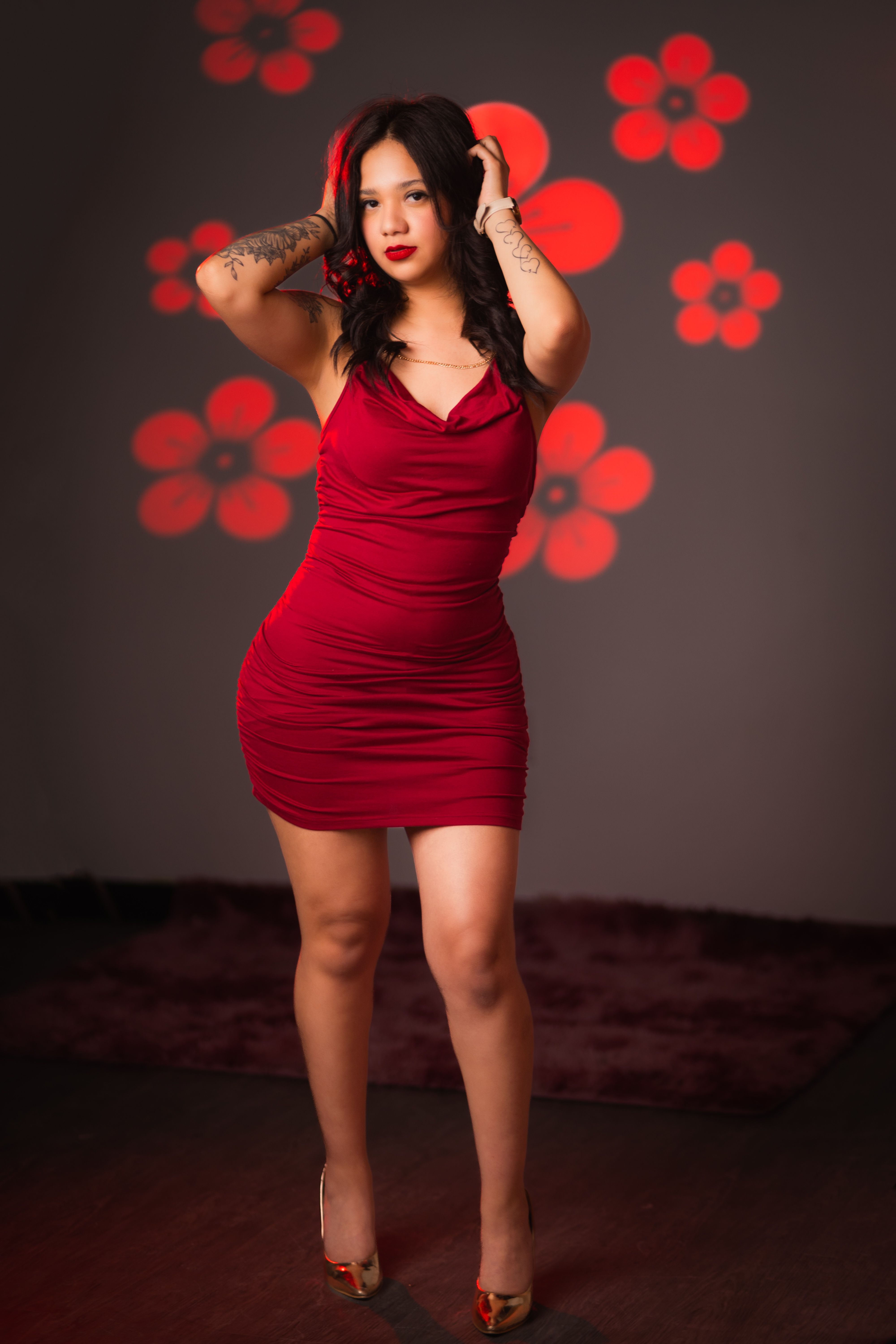 Stylish woman poses in a red dress with floral light projections on a dark background.