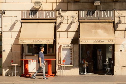 Free A man walks by Il Delfino cafe in daylight, showcasing its classic facade. Stock Photo