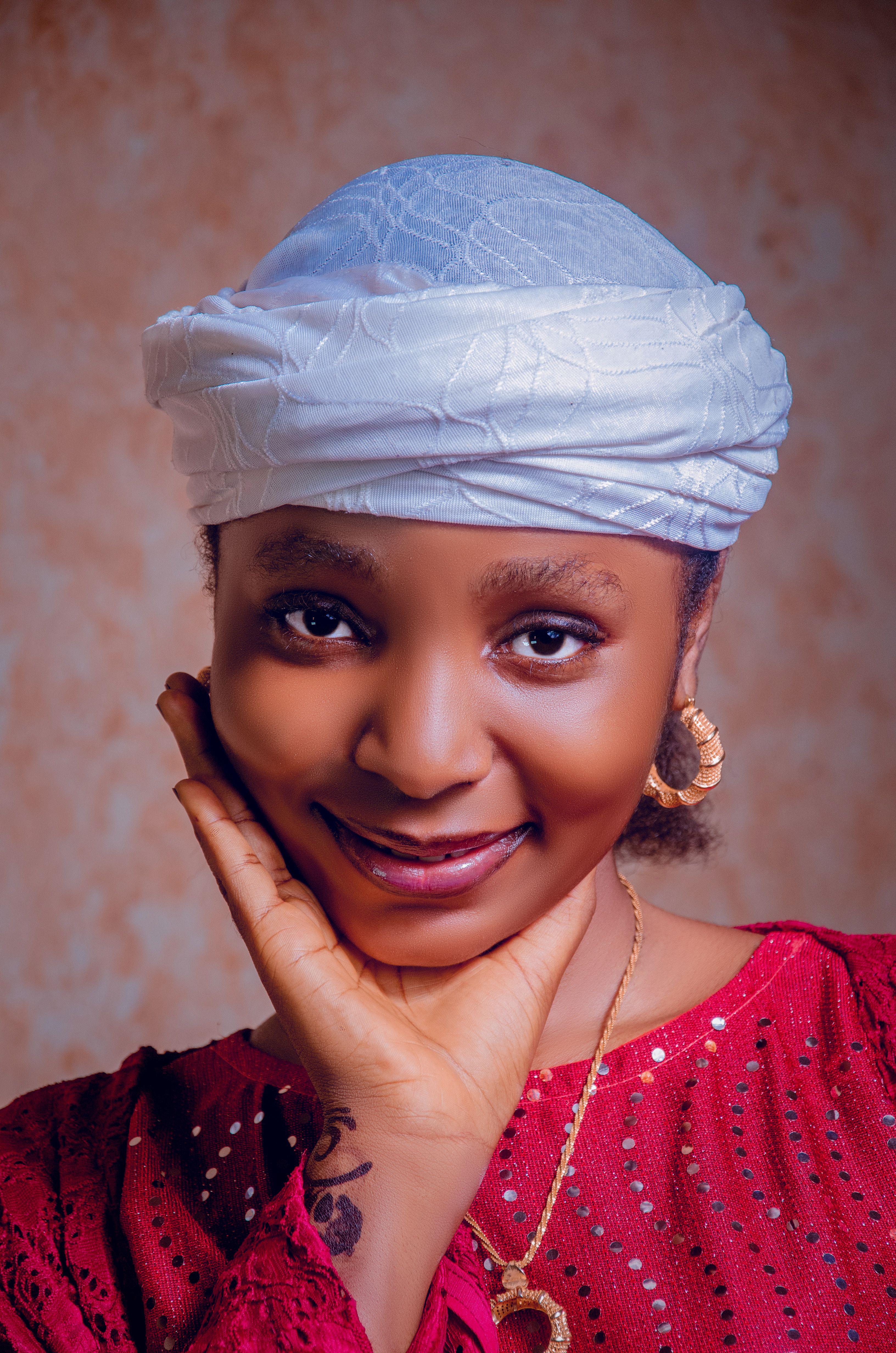 A young African woman in a red outfit and white hijab smiling warmly at the camera.