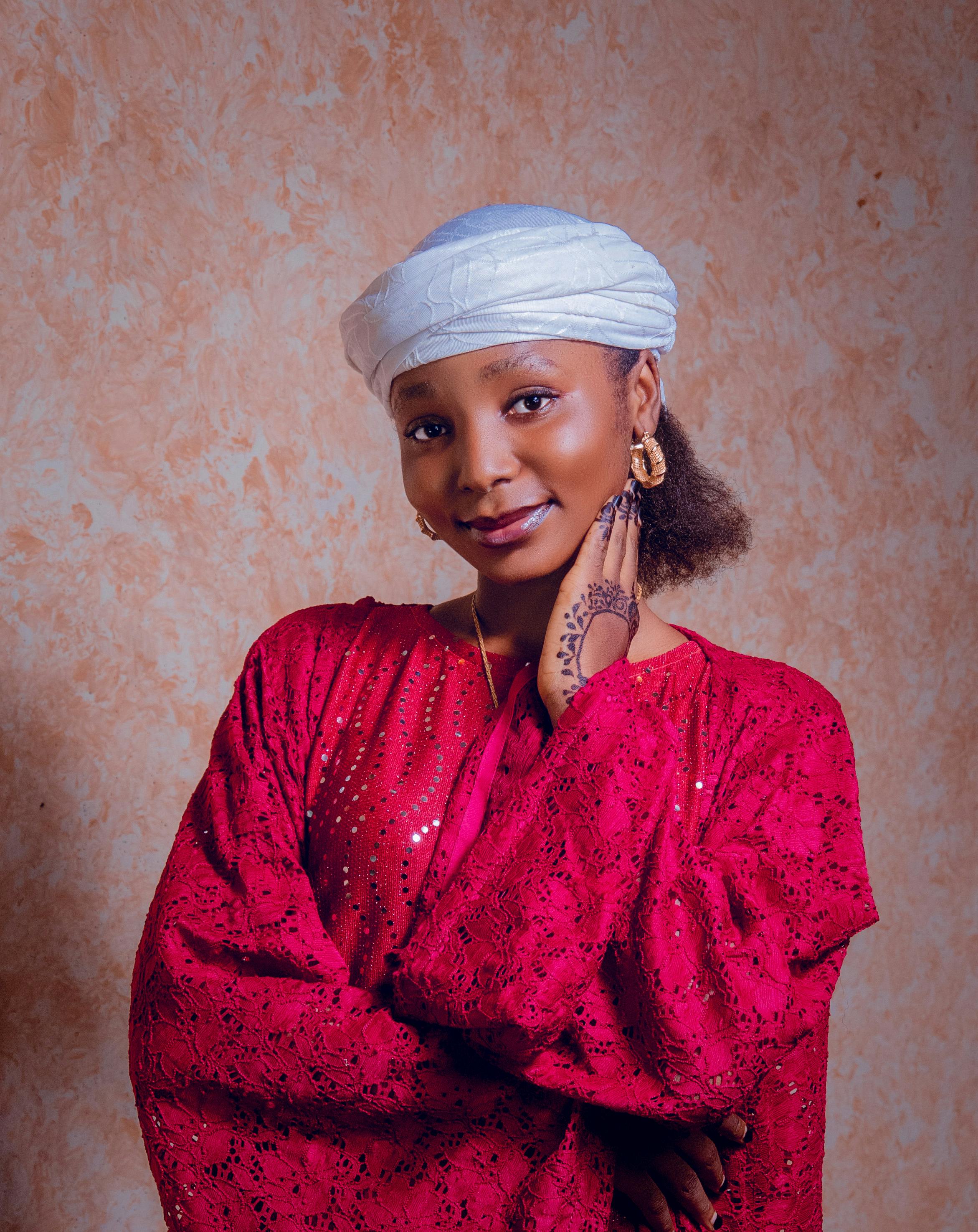 Portrait of a woman in vibrant red clothing with a henna design, smiling warmly.