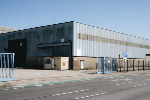 Free View of a large industrial warehouse in Dunkerque, showcasing its metal structure and broad entrance. Clear sky day. Stock Photo
