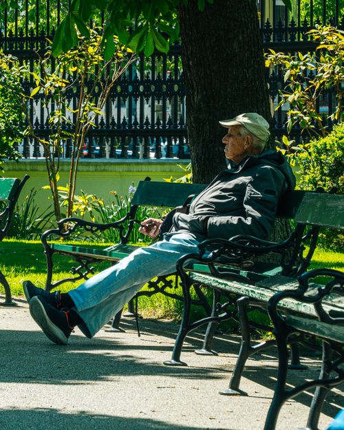 Free Elderly man enjoying a sunny day on a park bench surrounded by greenery. Stock Photo