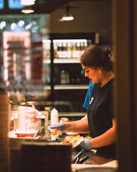 A focused moment of a young woman preparing food in a busy kitchen setting.