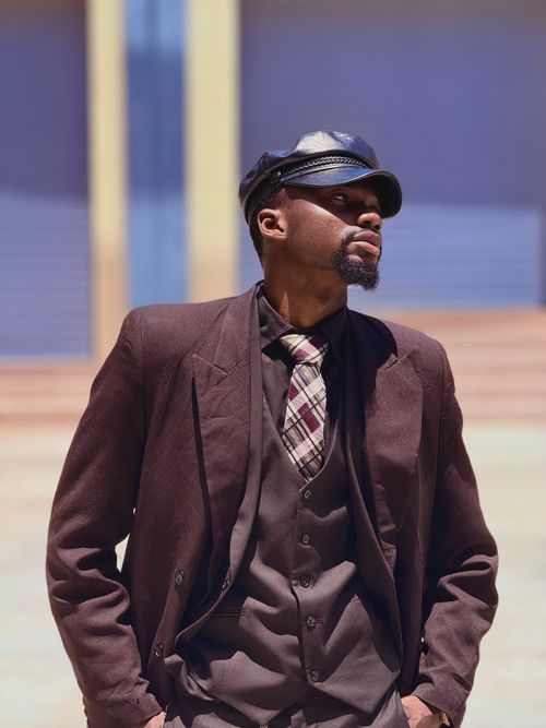 Free Portrait of a stylish man outdoors in Zaria, Nigeria, wearing a classic brown suit and leather cap. Stock Photo