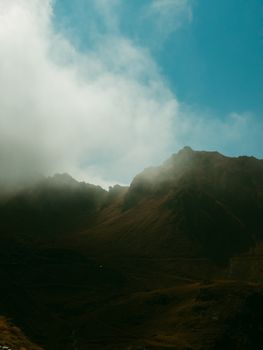 Captivating mist over a Transylvanian mountain peak with dramatic clouds and clear sky.