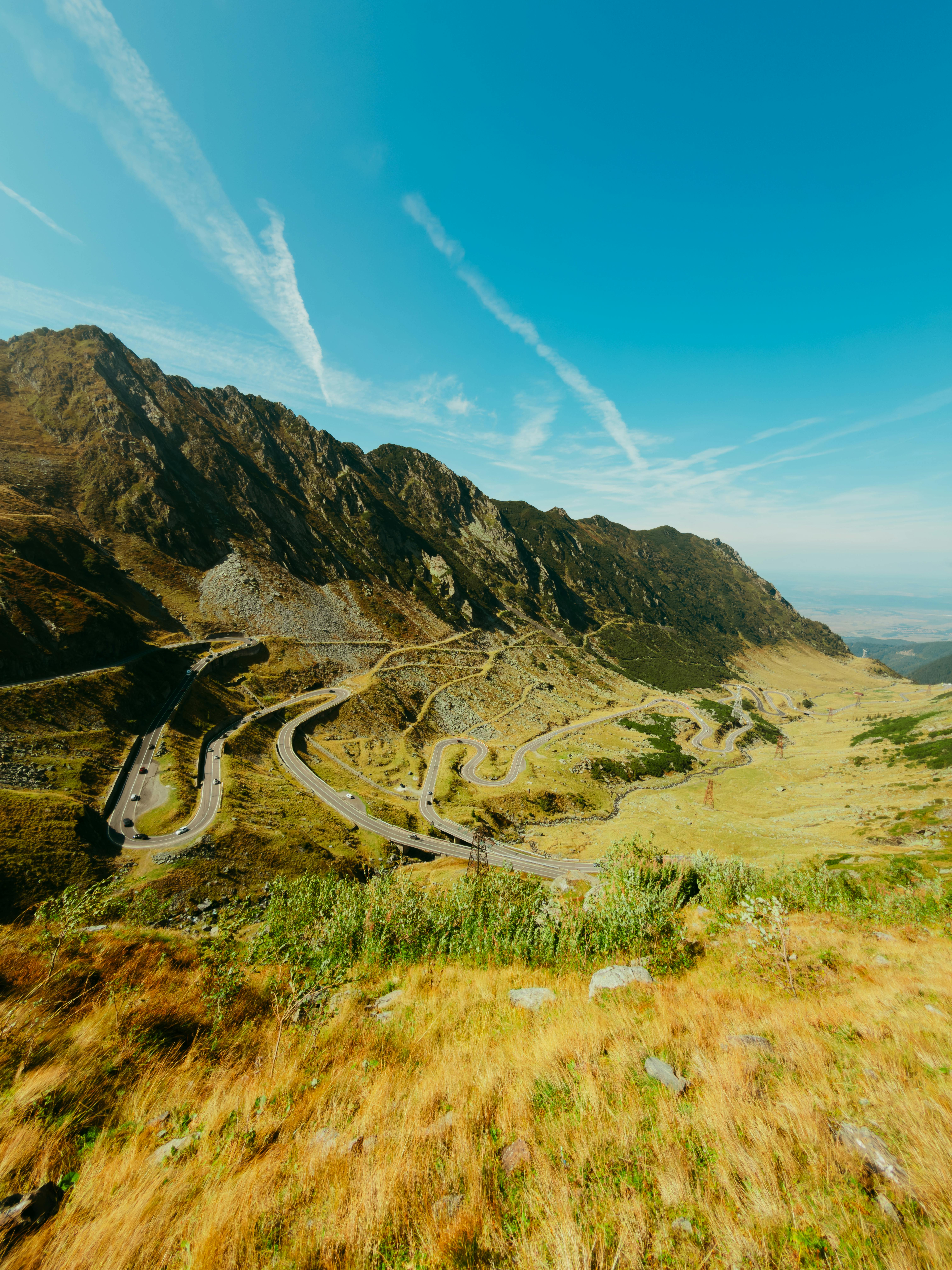Breathtaking aerial view of Transfagarasan Highway curving through the majestic Carpathian Mountains under a clear blue sky.