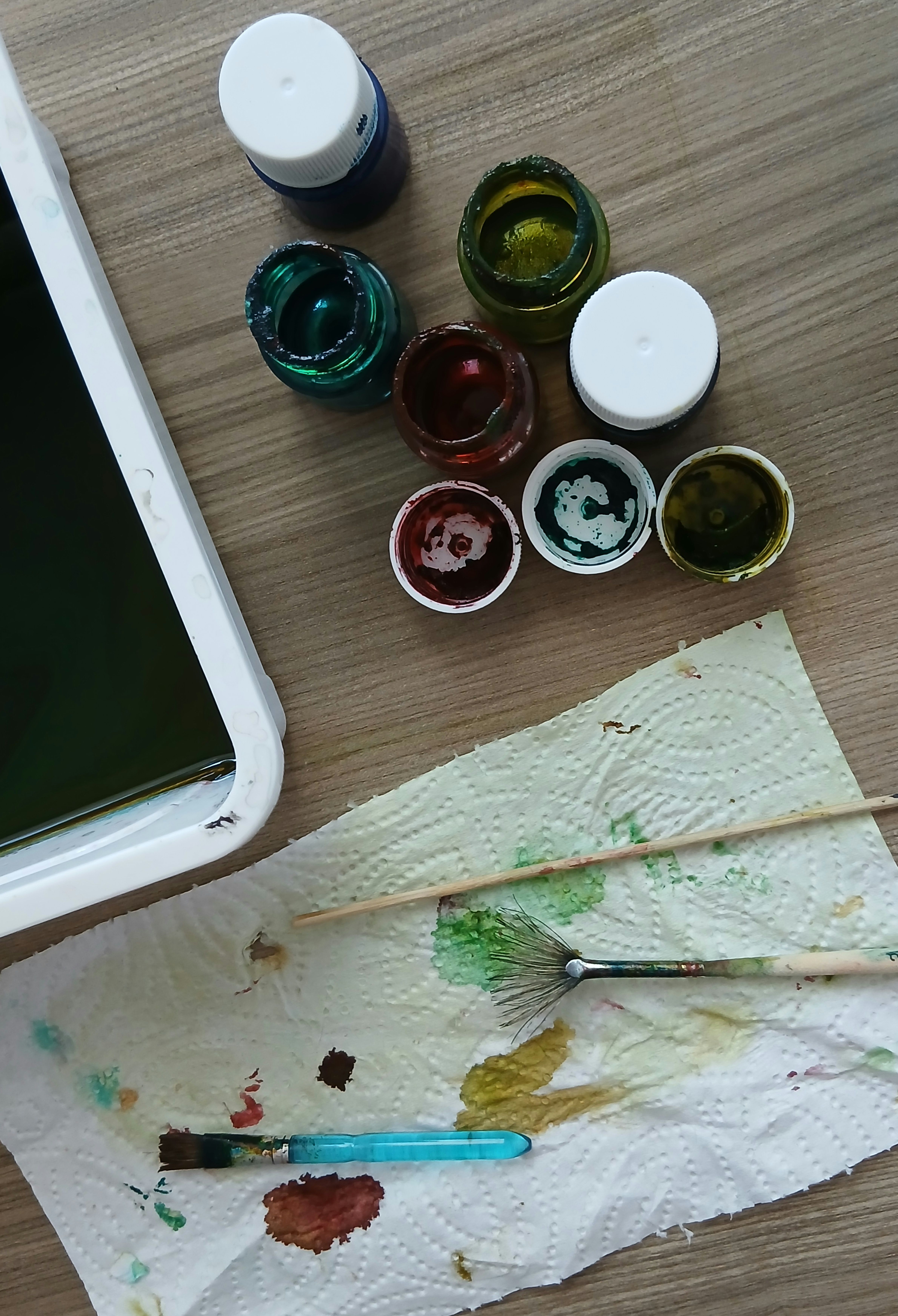 A table setup with all the necessary supplies for spork leaf art: sporks, acrylic paints in fall colors, paper, paint palette, and brushes.