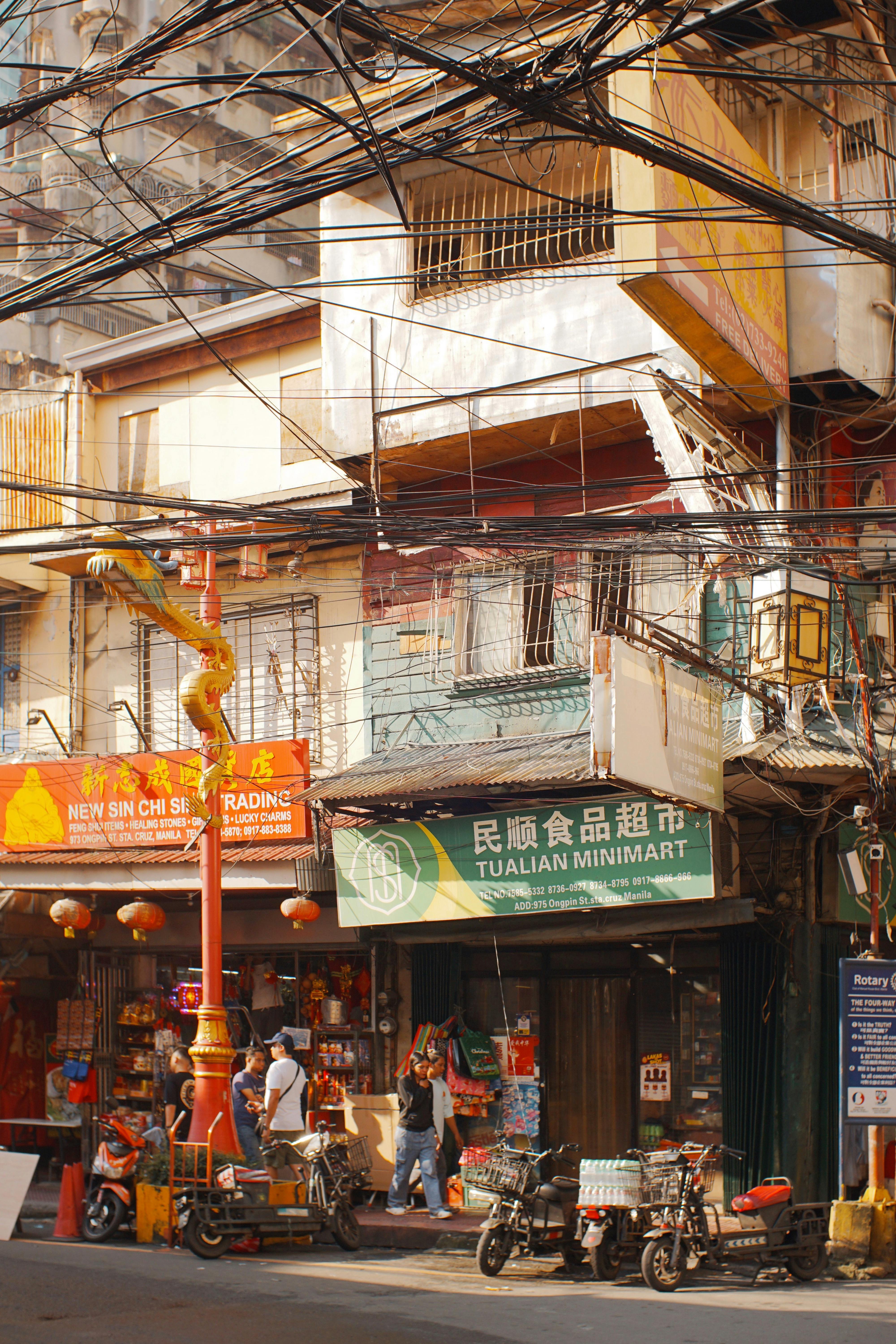 A bustling street view in Chinatown featuring shops, people, and scooters.