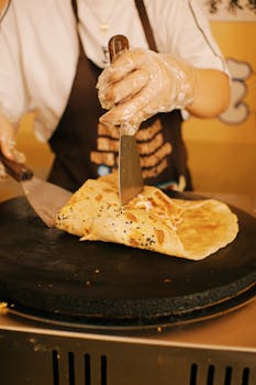Close-up of street vendor preparing a savory crepe on a hot griddle.