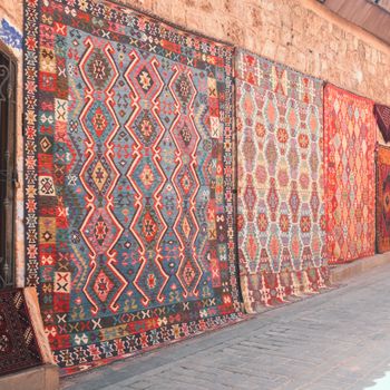Colorful traditional rugs with intricate patterns displayed on an outdoor wall, ideal for decor enthusiasts.
