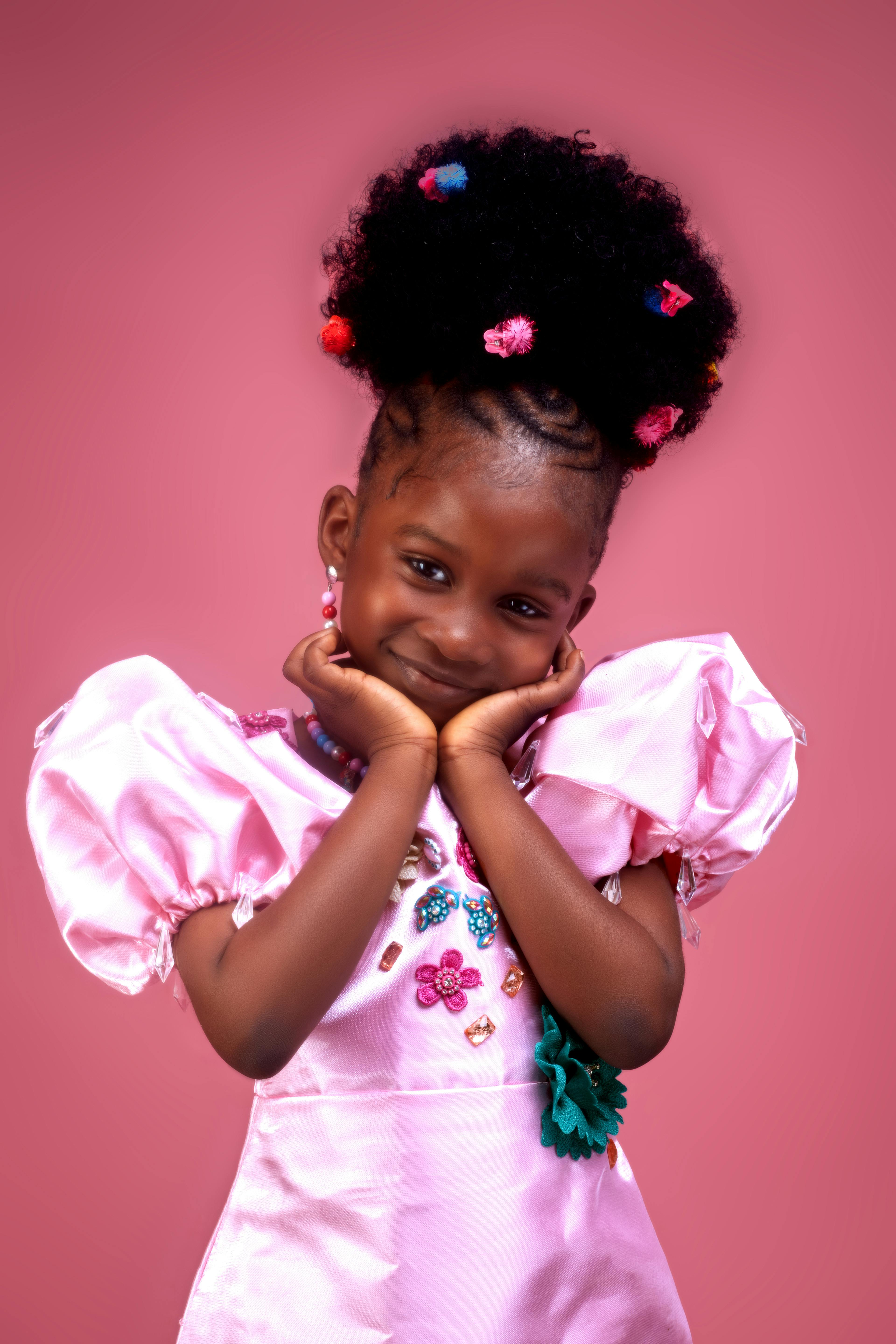 Adorable young girl smiling in pink dress with colorful hair accessories.