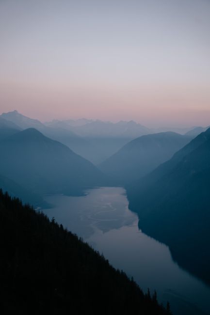 Peaceful view of a mountain valley and river at dusk with soft colors.