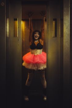 A gothic clown in vibrant makeup and costume inside a dimly lit elevator, capturing a spooky Halloween vibe.