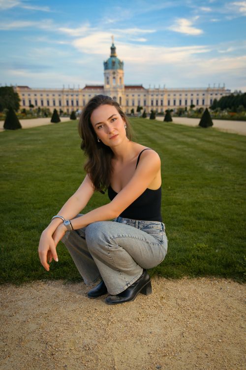 Free Woman posing confidently in front of Berlin's Charlottenburg Palace at sunset. Stock Photo