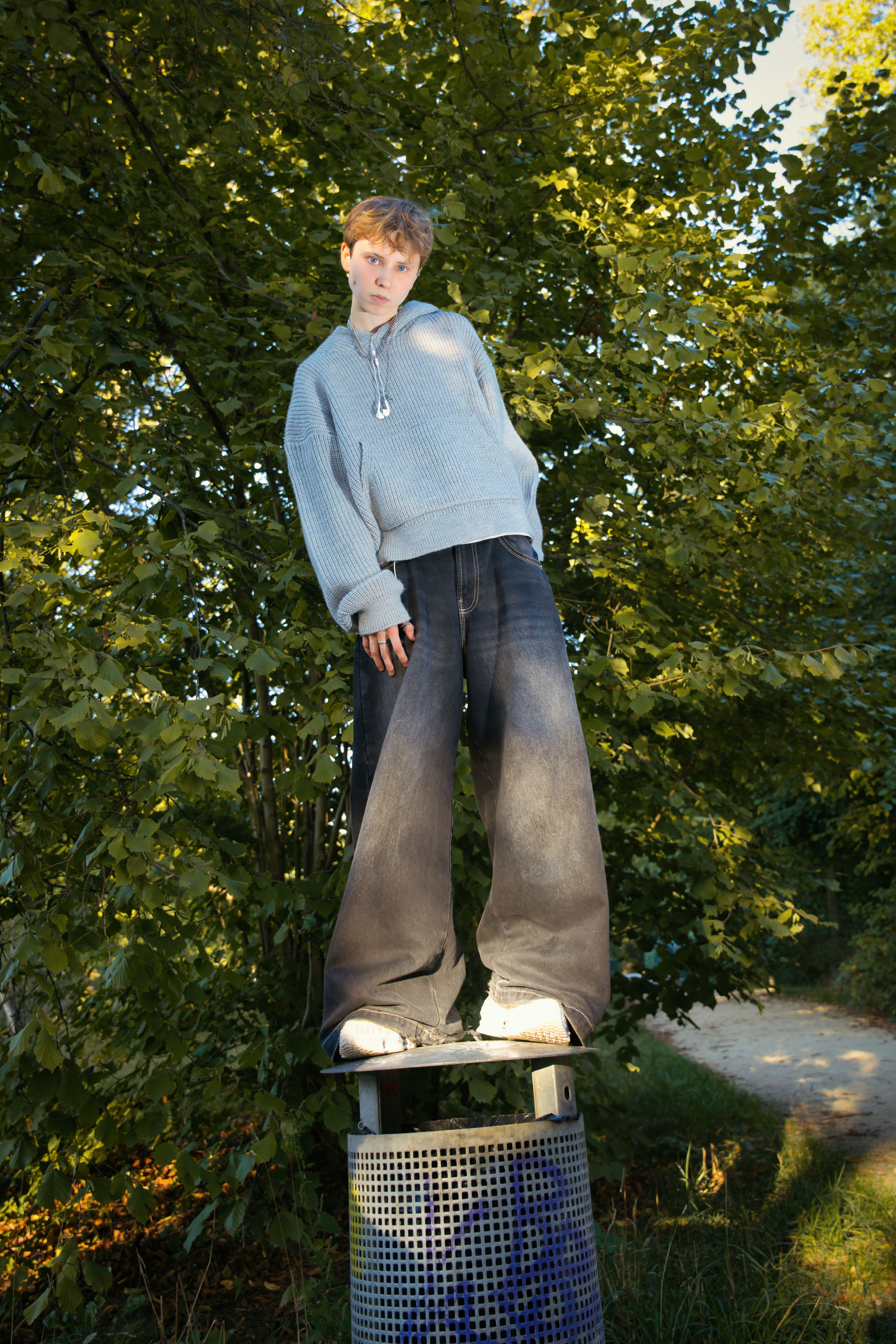 Young person in trendy attire posing outside on a sunny day in Berlin park.