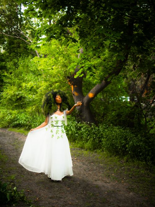 Free Woman in a flowing white dress walking gracefully in a lush green forest. Stock Photo