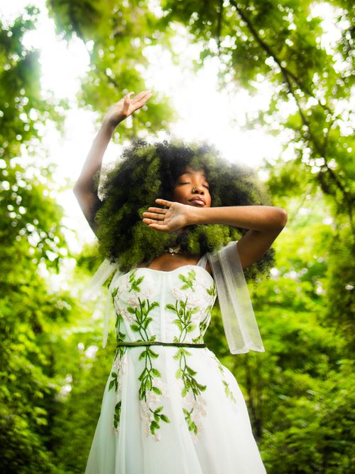 Free Graceful woman posing in floral dress amidst lush green woods, exuding elegance. Stock Photo