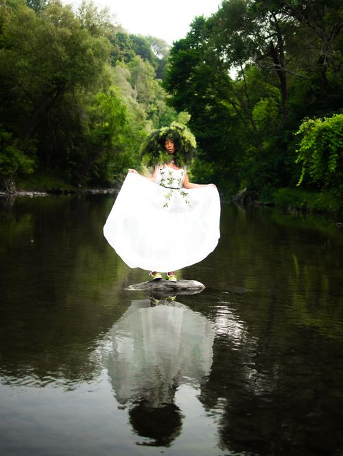 Free Elegant woman in a white dress stands on a rock in the forest, reflecting in the water. Stock Photo