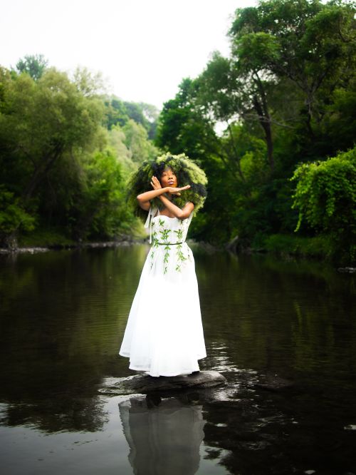 Free A woman in a white dress poses elegantly by a serene river amid lush greenery. Stock Photo