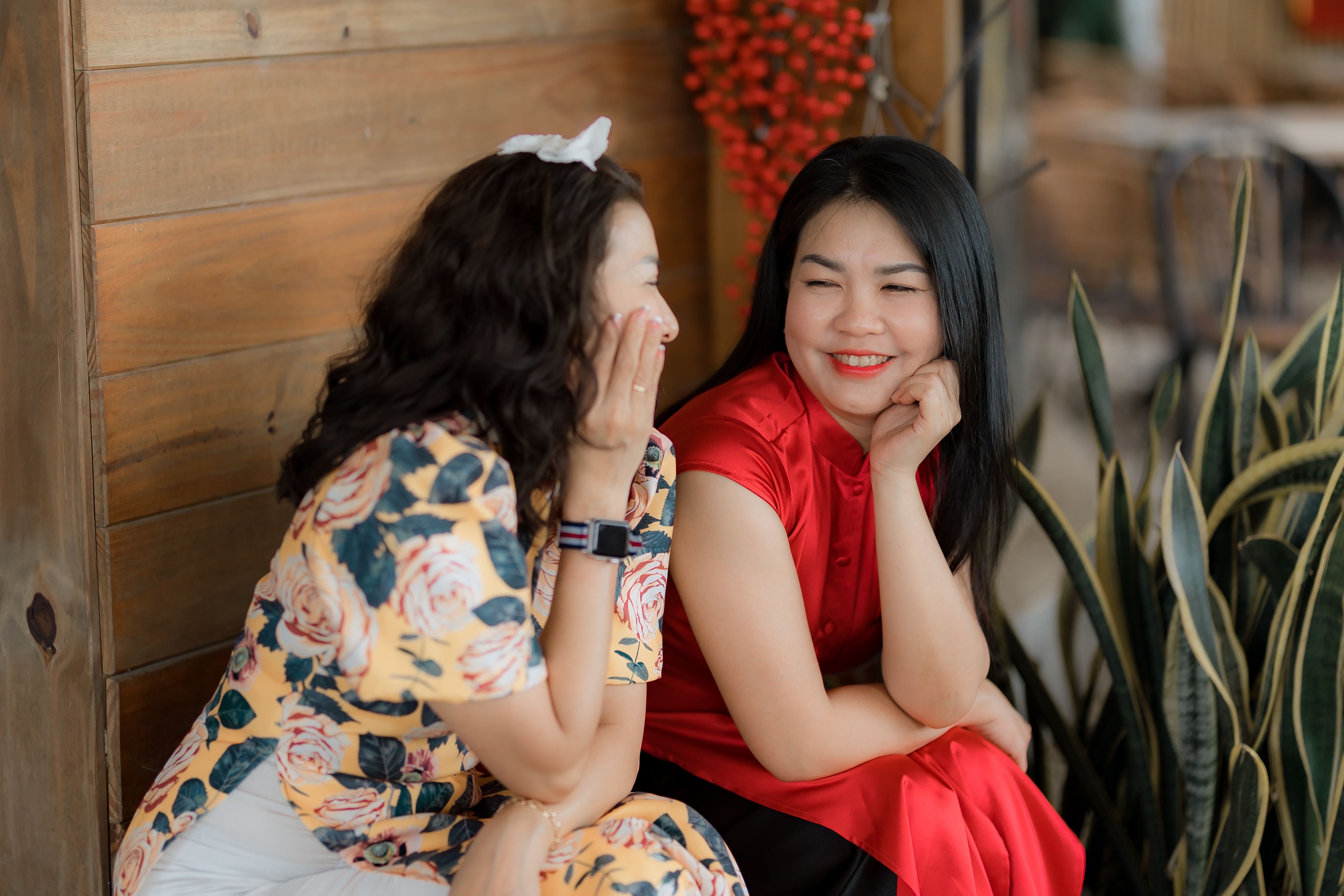 Two women enjoying a warm conversation indoors, dressed in floral and red attire.