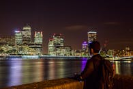 夜晚，一名男子站在泰晤士河畔，欣赏着灯火通明的摩天大楼和充满活力的伦敦天际线