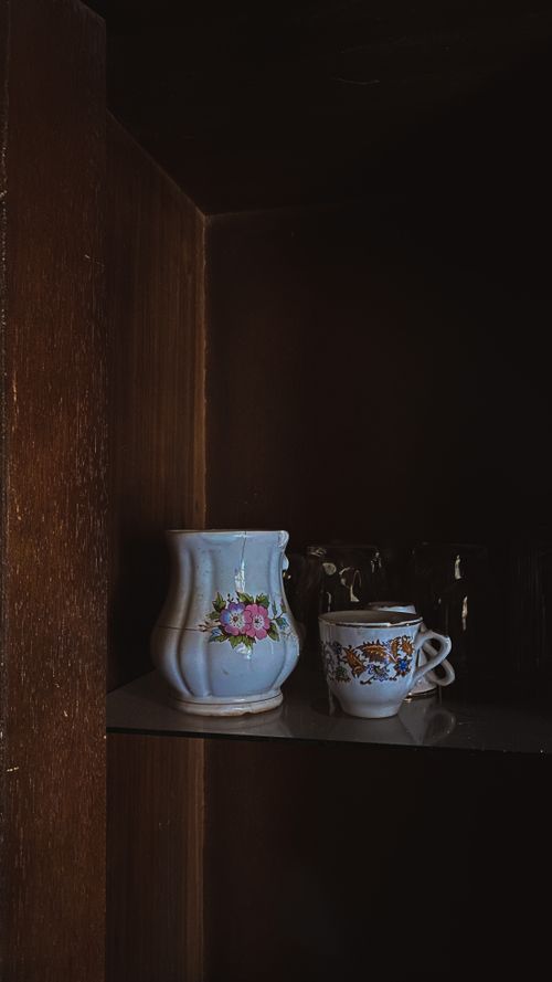Free A vintage ceramic vase and a floral teacup elegantly displayed on a dark wooden shelf. Stock Photo
