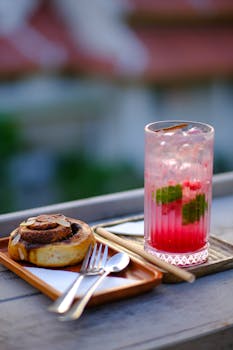 A cinnamon roll and refreshing drink served on a wooden table in Hue, Vietnam, outdoors.