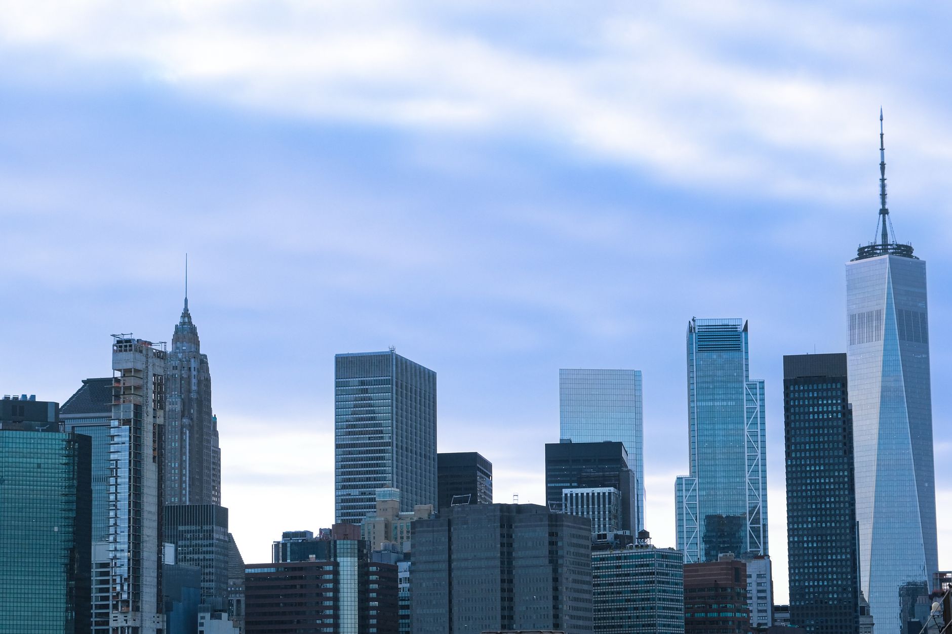 Dramatic view of New York City's skyline featuring One World Trade Center against a cloudy sky.