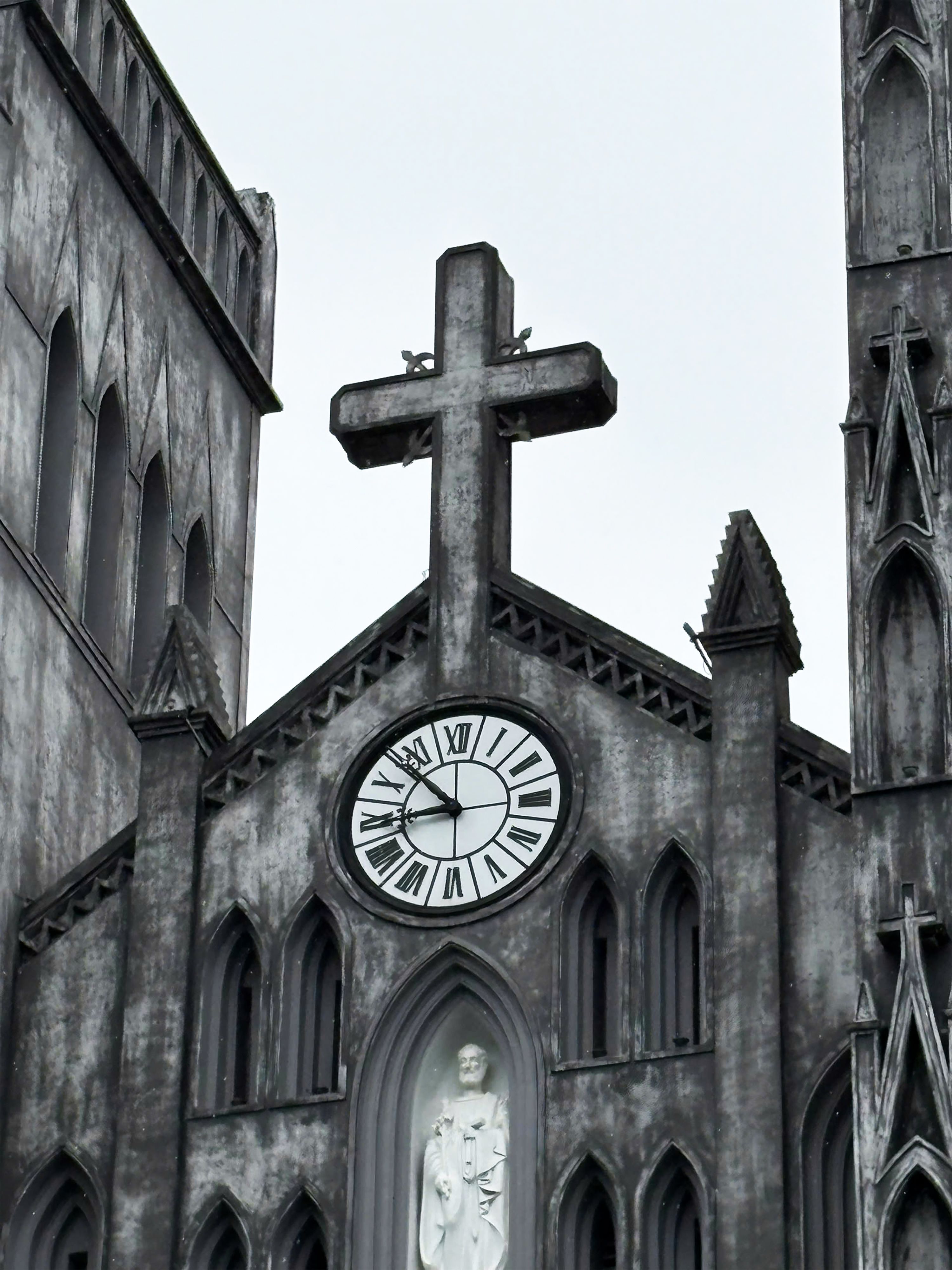 Close-up of the gothic facade of St. Joseph's Cathedral in Hanoi, featuring a clock and cross.