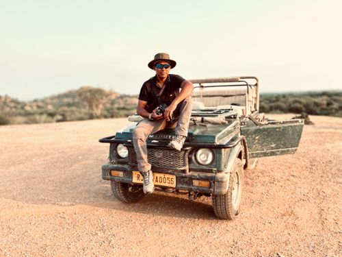 Free A man in sunglasses sits on a jeep in a dry, rugged landscape, exuding adventure. Stock Photo