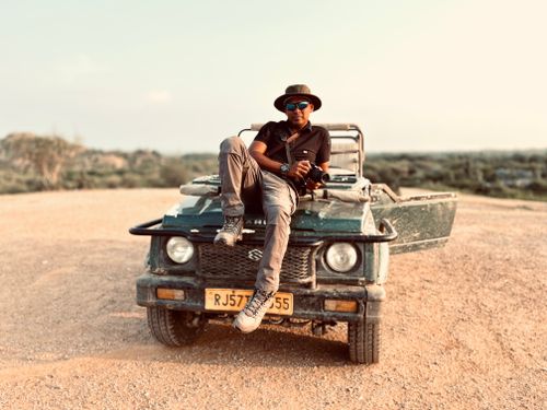 Free Man sitting on a jeep in a desert setting with a relaxed pose, wearing sunglasses and a hat. Stock Photo