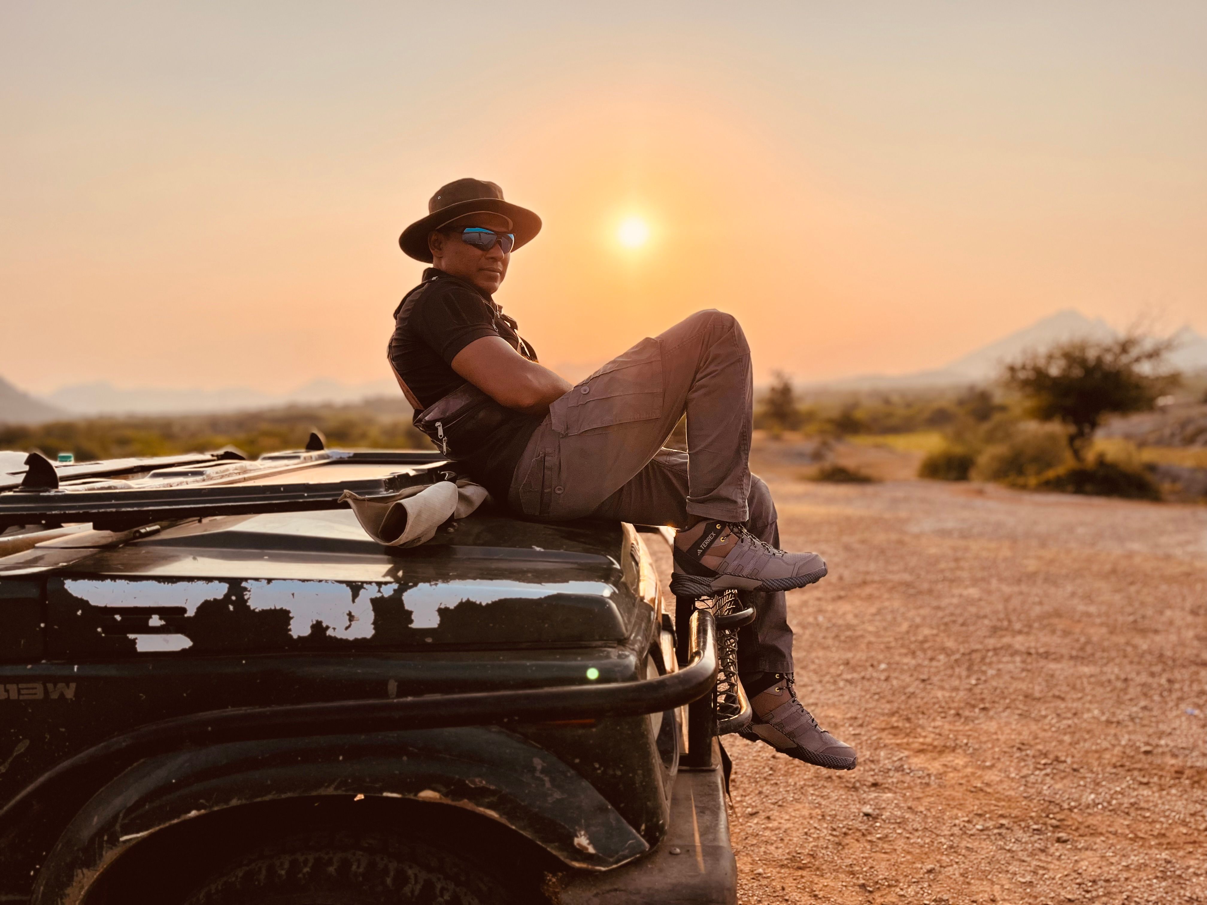 Adventure enthusiast relaxing on a Jeep during a stunning sunset in the wilderness.