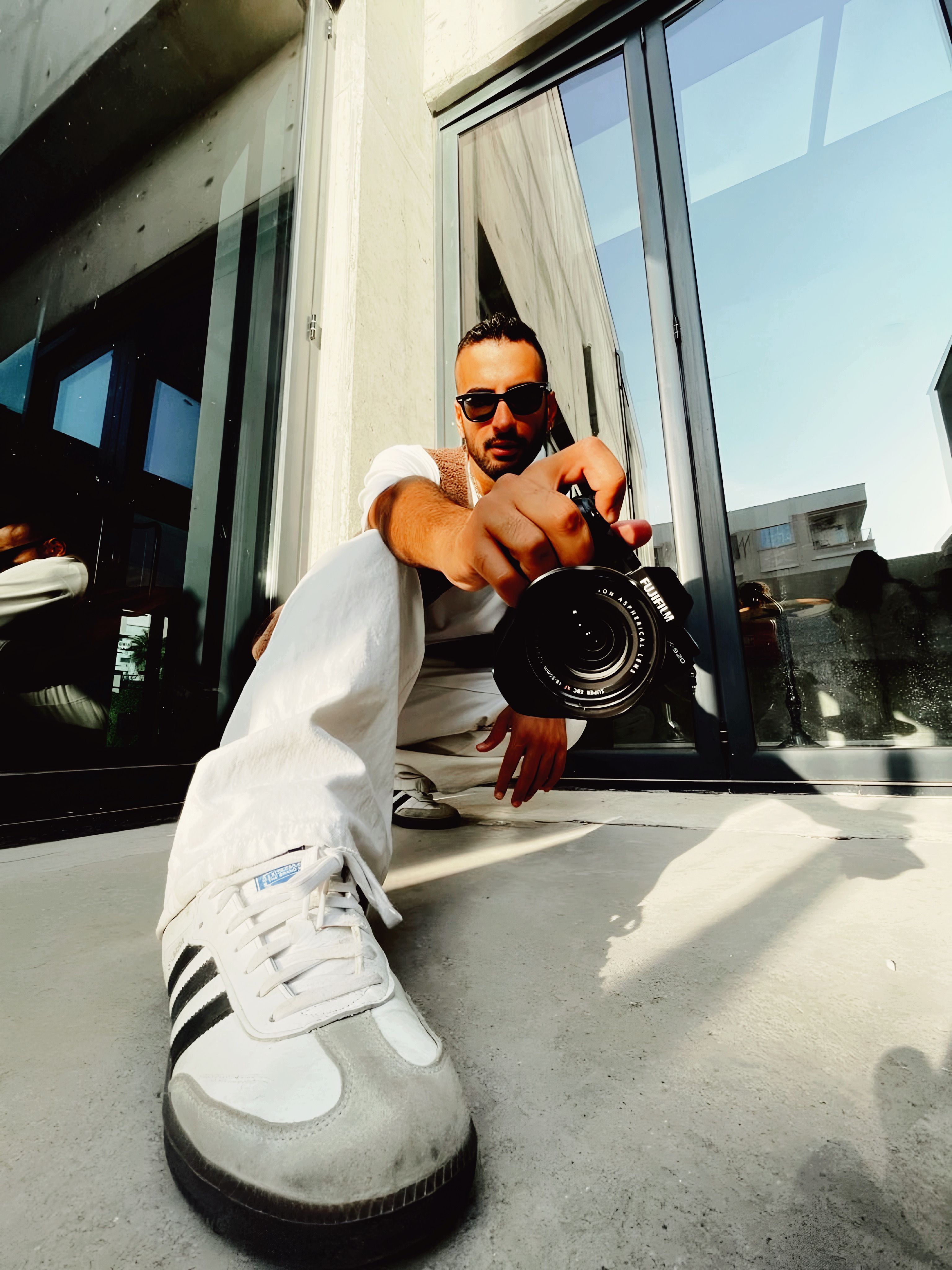 Low angle view of a stylish adult male photographer holding a camera outdoors.