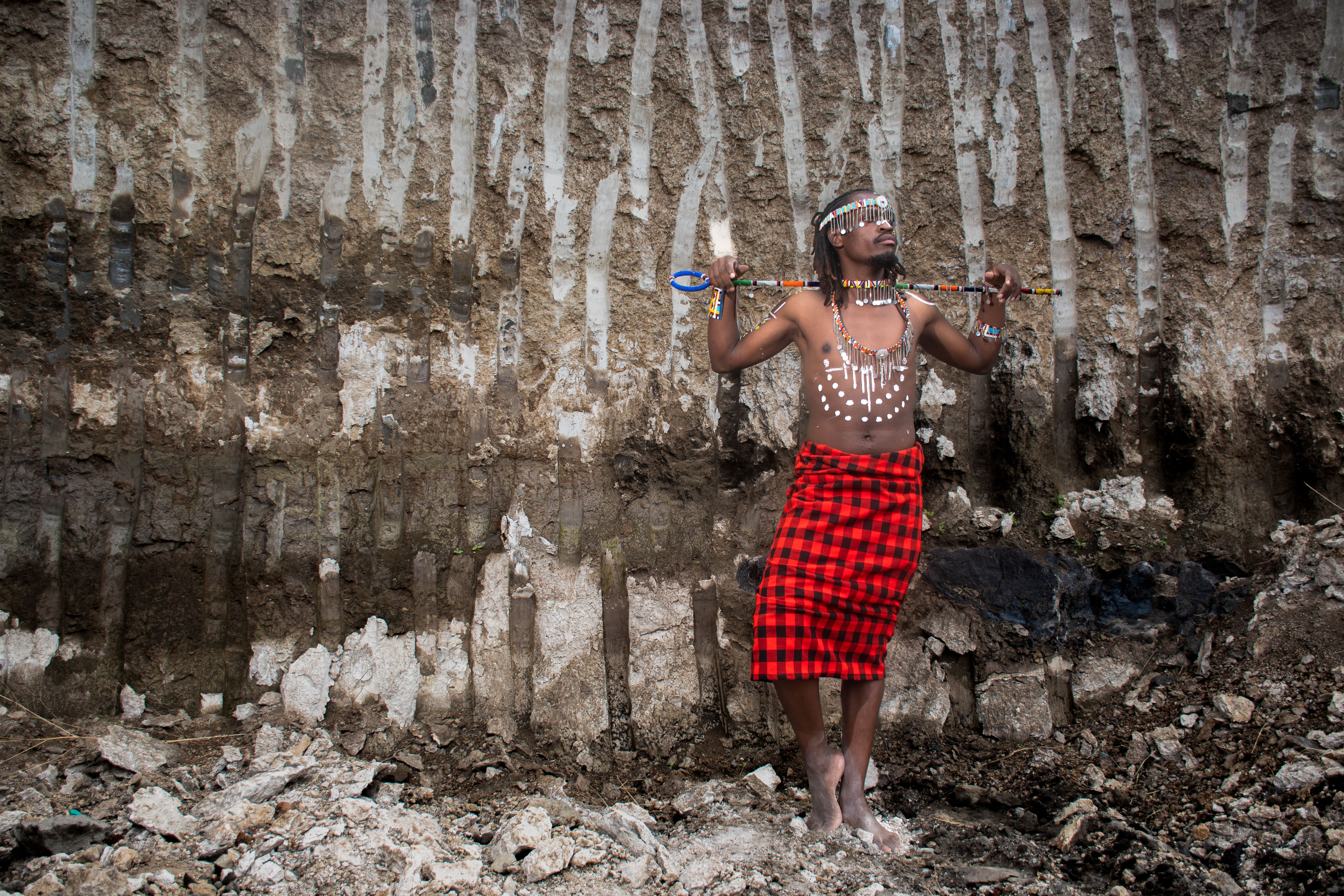 Cultural portrait of a man in tribal attire with spear in front of a geological formation.