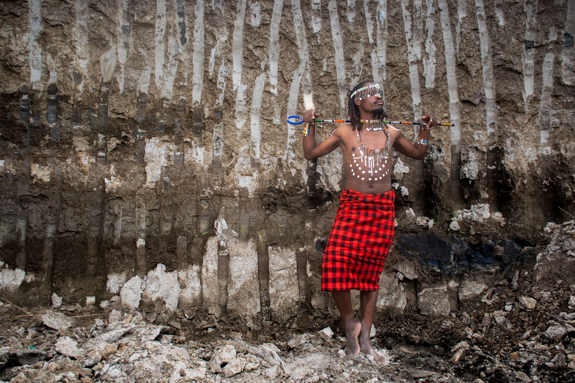 Cultural portrait of a man in tribal attire with spear in front of a geological formation.