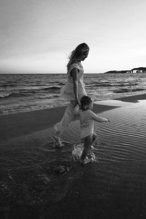 Free A serene black and white photo of a mother and child walking along a beach at sunset. Stock Photo