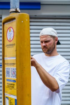 Man interacts with a yellow kiosk in an urban setting, focused on display.